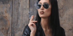 girl in a leather jacket and sunglasses smoking a cigarette